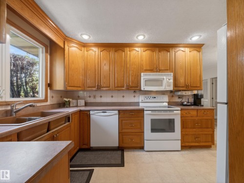 Kitchen featuring wood cabinetry, white appliances, recessed lighting, and a window with exterior tree views - 18416 90 Avenue, Edmonton, AB 
