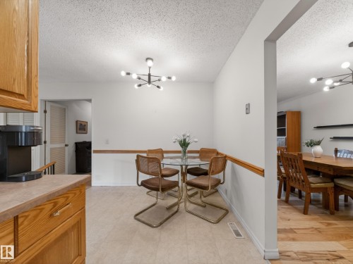 Eat-in kitchen area featuring a modern sputnik chandelier, wood-finish baseboard and chair rail trim, and neutral tile flooring - 18416 90 Avenue, Edmonton, AB 