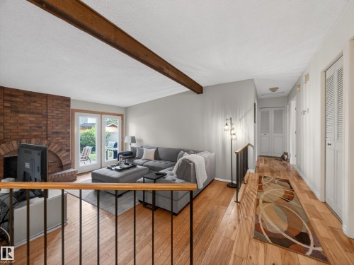 Open-concept living space featuring wood-finish flooring, a brick fireplace, and exposed wood beam - 18416 90 Avenue, Edmonton, AB 