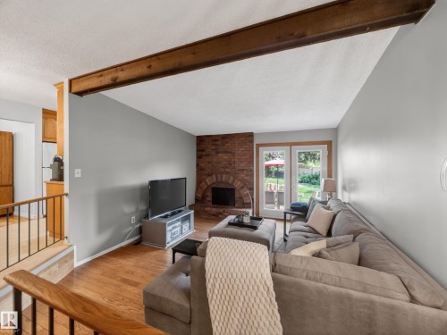 Living room featuring a prominent exposed wood beam, wood-finish flooring, and a brick fireplace - 18416 90 Avenue, Edmonton, AB 