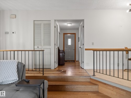 Split-level entryway featuring wood-finish flooring and a partial black metal and wood railing - 18416 90 Avenue, Edmonton, AB 