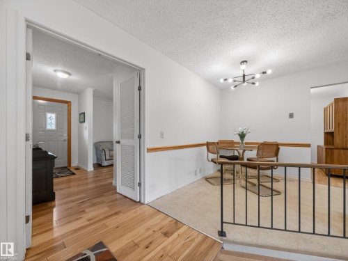 Dining area with a contemporary chandelier, tile flooring, and a half-wall featuring a wood rail - 18416 90 Avenue, Edmonton, AB 