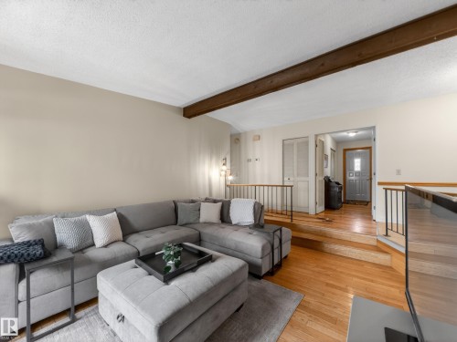 Living area with wood-finish flooring, a prominent exposed wood beam, light-toned walls, and black metal railings - 18416 90 Avenue, Edmonton, AB 