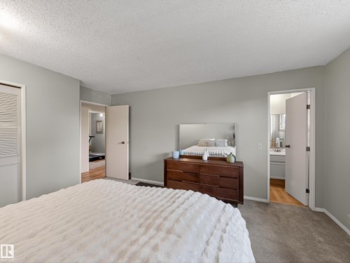 Carpeted bedroom featuring light gray walls, a louvered bi-fold closet door, and a recessed doorway revealing wood-finish flooring - 18416 90 Avenue, Edmonton, AB 