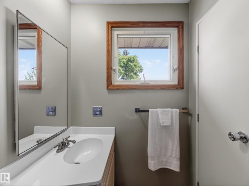 Bathroom featuring a single vanity with an integrated sink, polished chrome faucet, and a large wall-mounted mirror - 18416 90 Avenue, Edmonton, AB 