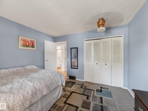 Bedroom featuring textured carpet flooring, bi-fold louvered closet doors, and a ceiling fan with integrated lighting - 18416 90 Avenue, Edmonton, AB 