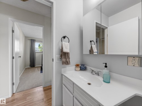 Bathroom vanity featuring a white countertop with integrated sink, chrome faucet, and a wall-mounted medicine cabinet with mirrored doors - 18416 90 Avenue, Edmonton, AB 