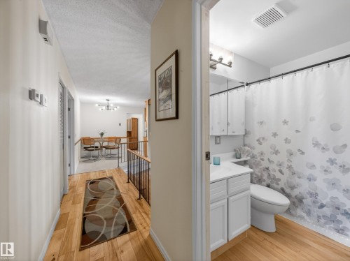 Bright full bathroom featuring a white vanity, white toilet, and wood-finish flooring - 18416 90 Avenue, Edmonton, AB 