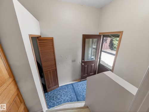 Entryway featuring a dark wood-finish door with glass inset, an open screen door, and a louvered wood-finish closet door - 18416 90 Avenue, Edmonton, AB 