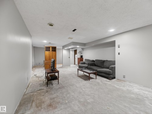 Spacious room featuring light gray walls, textured ceiling, recessed lighting, and a built-in wood-finish cabinet with glass inserts - 18416 90 Avenue, Edmonton, AB 