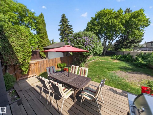 Expansive wood-finish deck with surrounding mature trees, a wood privacy fence, and a lush lawn area - 18416 90 Avenue, Edmonton, AB 