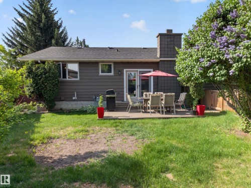 Rear exterior featuring a concrete patio, sliding glass door, and a shingle-clad chimney - 18416 90 Avenue, Edmonton, AB 