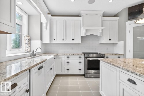 Large White Cabinet Kitchen featuring Granite Counters, Sub-Zero Refrigerator, Dishwasher (2025), Garburator (2025), Electric Stove (2026), Large Walk Through Pantry, and Prep Sink in Island - 5016 213 Street, Edmonton, AB 