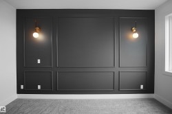 Accent wall featuring dark paneling with decorative trim, two wall-mounted sconces with spherical glass shades, and light gray carpeting - 