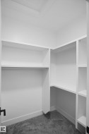 Walk-in closet featuring white built-in shelving, hanging rods, and gray carpeting - 