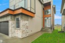 Contemporary exterior featuring a modern entry door with frosted glass panels, stone veneer accents, wood-finish siding, and a two-car garage - 142 Edgewater Circle, Leduc, AB 