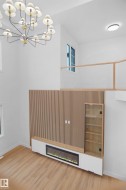 Open-concept interior featuring light wood-finish flooring, a contemporary chandelier, and a built-in media console with an integrated fireplace - 