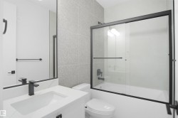 Bathroom featuring a tub/shower combination with black-framed glass sliding doors, a vanity with an integrated sink, a large mirror, and matte black fixtures - 