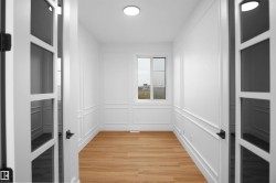 French doors with black hardware open to a room featuring light wood-finish flooring, white paneled walls, and a recessed ceiling light - 