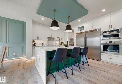 Gourmet kitchen featuring a waterfall island, integrated stainless steel appliances, custom cabinetry, wood-finish flooring, and decorative wall paneling - 16607 8 Street, Edmonton, AB 
