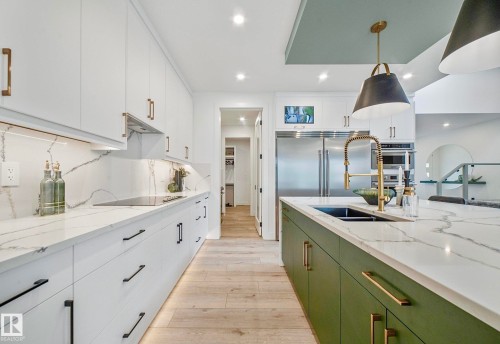 Kitchen featuring a large island with a black sink and brass faucet, white cabinetry with black and brass hardware, stainless steel appliances, and light wood-finish flooring - 16607 8 Street, Edmonton, AB 