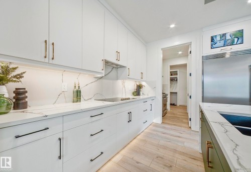 Kitchen featuring light wood-finish flooring, white cabinetry, integrated stainless steel appliances, and quartz countertops with a matching backsplash - 16607 8 Street, Edmonton, AB 