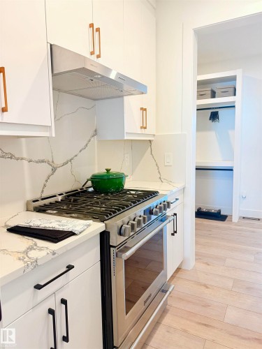 Modern kitchen featuring white cabinetry with contrasting hardware, stainless steel range with matching range hood, and a stone-finish countertop with a distinctive veining pattern - 16607 8 Street, Edmonton, AB 