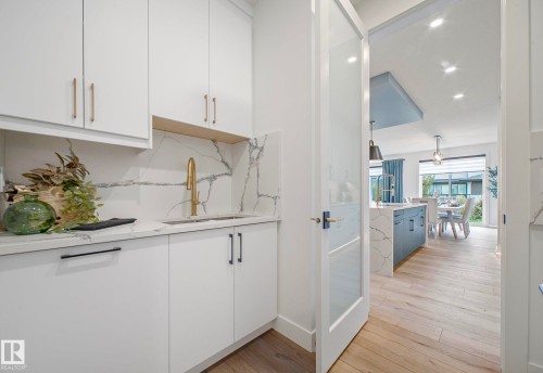 Utility area featuring white cabinetry with gold-tone hardware, a gold-tone faucet, and a stone-finish backsplash - 16607 8 Street, Edmonton, AB 