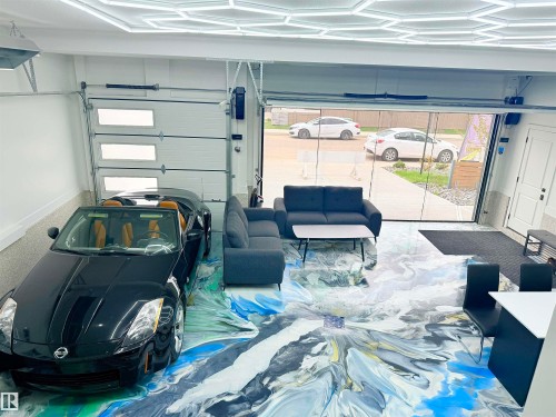 Spacious garage featuring a full glass panel door, an additional insulated garage door with rectangular window inserts, and an abstract multi-color epoxy floor finish - 16607 8 Street, Edmonton, AB 