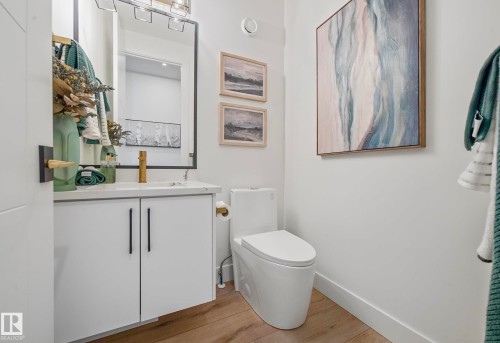 Powder room featuring a floating white vanity with black hardware, gold-tone faucet, and wood-finish flooring - 16607 8 Street, Edmonton, AB 