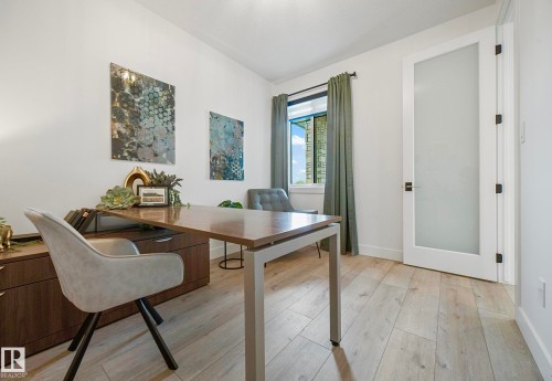 Room featuring wood-finish flooring, a contemporary desk with integrated storage, and a window with exterior views - 16607 8 Street, Edmonton, AB 