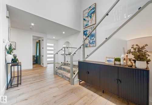 Bright entryway featuring light wood-finish flooring, a contemporary staircase with glass railings and carpeted treads, and a modern front door with horizontal frosted glass inserts - 16607 8 Street, Edmonton, AB 