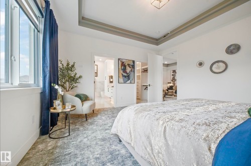 Spacious bedroom featuring a tray ceiling with recessed lighting, large window with roller shades, plush patterned carpeting, and double door frames opening to additional rooms - 16607 8 Street, Edmonton, AB 