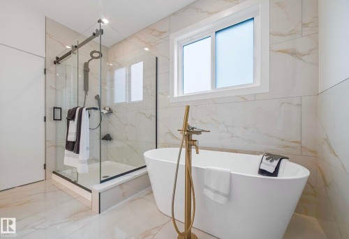 Freestanding soaking tub with a floor-mounted gold-tone faucet, complemented by a glass-enclosed shower with black hardware - 16607 8 Street, Edmonton, AB 
