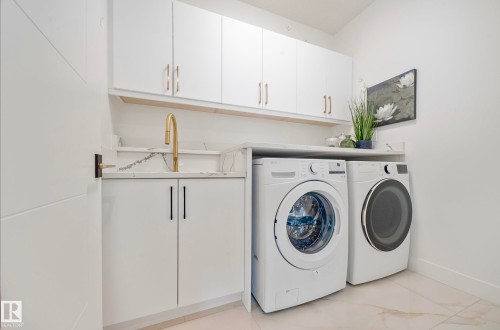 Laundry area featuring white cabinetry with gold-tone hardware, a gold-tone faucet, a white countertop with a matching backsplash, and light-toned tile flooring - 16607 8 Street, Edmonton, AB 