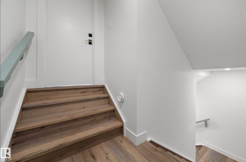 Wood-finish staircase with a contemporary white handrail, leading to a modern white door with dark hardware - 16607 8 Street, Edmonton, AB 