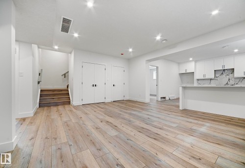 Open-concept living area featuring wood-finish flooring, recessed lighting, and a kitchen with white cabinetry - 16607 8 Street, Edmonton, AB 