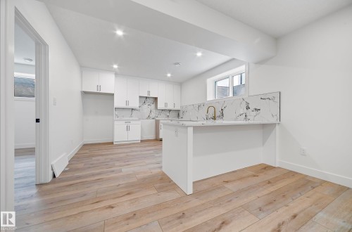 Modern kitchen featuring white cabinetry, a waterfall-edge island, a gold-finish faucet, and a patterned backsplash - 16607 8 Street, Edmonton, AB 