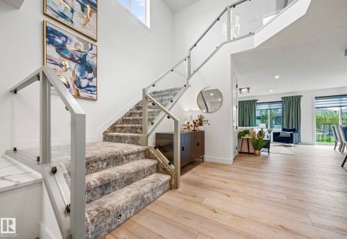 Entry foyer featuring a modern staircase with glass panel railings and carpeted treads, complemented by light wood-finish flooring - 16607 8 Street, Edmonton, AB 