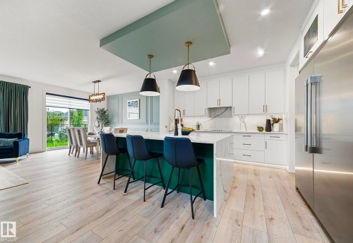Modern kitchen featuring a waterfall island with integrated seating, complemented by white cabinetry, a full-height backsplash, and light wood-finish flooring - 16607 8 Street, Edmonton, AB 