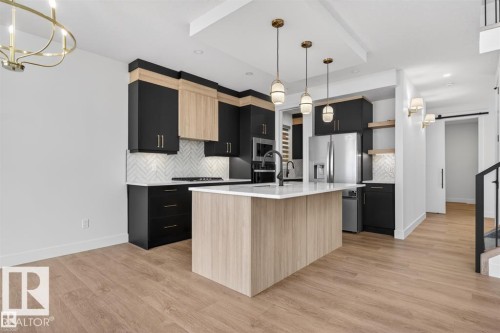 Modern kitchen featuring two-tone cabinetry, a central island with a white countertop, and stainless steel appliances - 19 Rosa Crescent, St. Albert, AB 