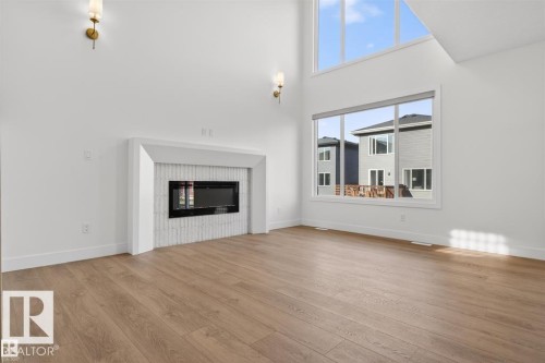 Spacious room featuring a contemporary fireplace with a white tile surround, wood-finish flooring, high ceilings, and large windows - 19 Rosa Crescent, St. Albert, AB 