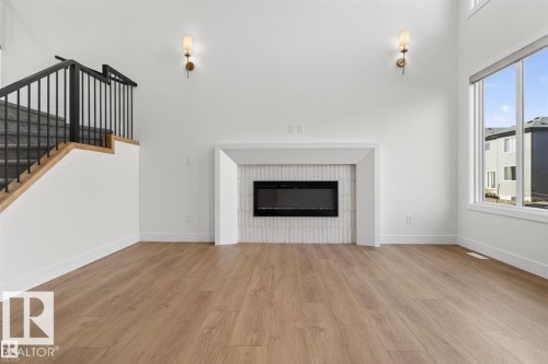 Spacious living area featuring high ceilings, wood-finish flooring, and a modern fireplace with a textured tile surround - 19 Rosa Crescent, St. Albert, AB 