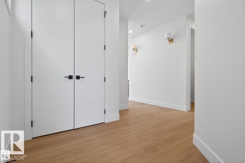 Hallway with wood-finish flooring, white walls, and contemporary double doors featuring matte black hardware - 19 Rosa Crescent, St. Albert, AB 