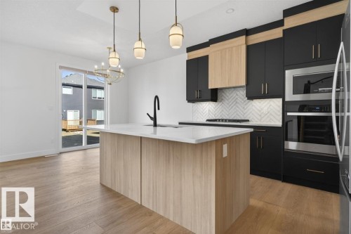 Modern kitchen featuring black and light wood-finish cabinetry, a central island with a solid surface countertop, stainless steel appliances, and a herringbone tile backsplash - 19 Rosa Crescent, St. Albert, AB 