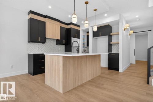 Modern kitchen featuring a central island with a light wood-finish base and a white countertop - 19 Rosa Crescent, St. Albert, AB 