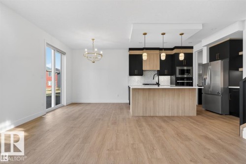Kitchen and living area featuring wood-finish flooring, a kitchen island with pendant lighting, dual-tone cabinetry, stainless steel appliances, and a sliding glass door - 19 Rosa Crescent, St. Albert, AB 