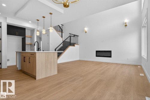 Open-concept living space with wood-finish flooring, a contemporary kitchen island with a white countertop, and an integrated linear fireplace - 19 Rosa Crescent, St. Albert, AB 