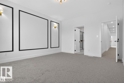 Spacious room featuring light gray carpeting, crisp white walls with black architectural trim, and two gold-toned wall sconces - 19 Rosa Crescent, St. Albert, AB 