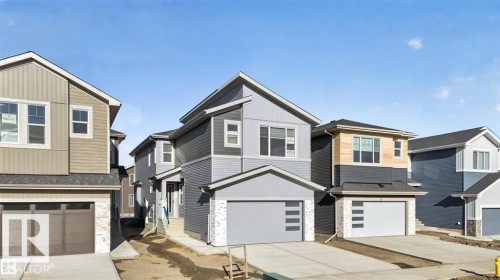Modern two-story residence featuring a striking blue and gray exterior, an integrated single-car garage, multiple windows, and a paved driveway - 19 Rosa Crescent, St. Albert, AB 